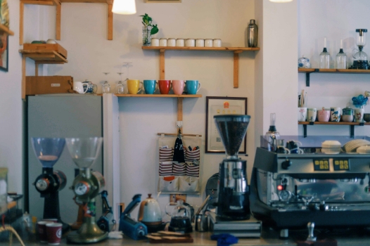 image of a coffee shop counter with a variety of equipment and shelves containing a variety of different colored coffee mugs